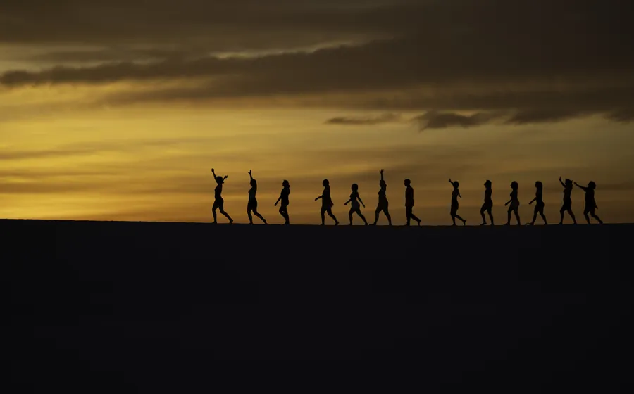 Grupo caminhando em fila pelas dunas dos Lençóis Maranhenses ao entardecer